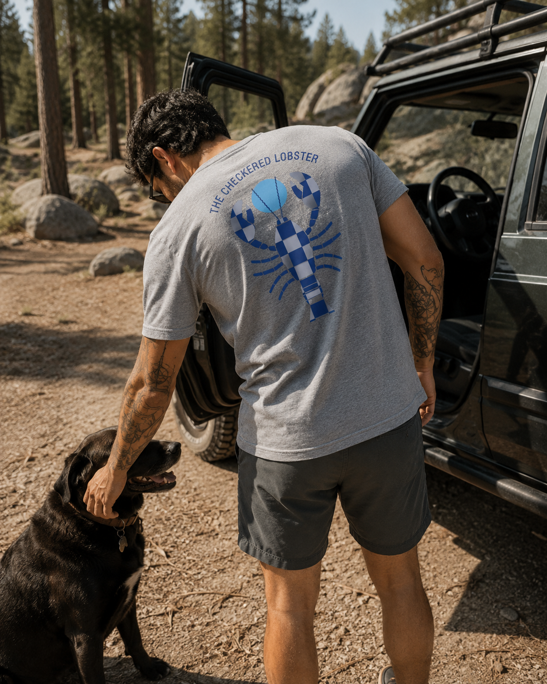Man with his dog beside a truck showing the full arched Checkered Lobster print on the back of the Heather Grey Men's Drift Tee